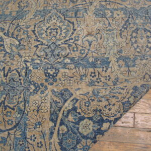 A distressed rug with blue and tan traditional patterns lies on rustic light brown wooden flooring.