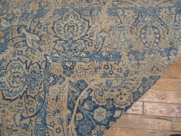 A distressed rug with blue and tan traditional patterns lies on rustic light brown wooden flooring.
