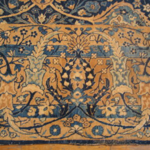 Detailed floral rug pattern in navy, teal, and golden tan rests close-up on a wooden floor.