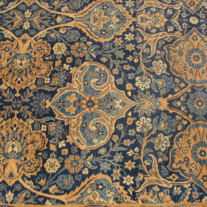 Close-up of a plush rug featuring an ornate floral pattern in navy blue and golden tan.