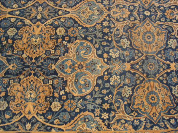 Close-up of a plush rug featuring an ornate floral pattern in navy blue and golden tan.