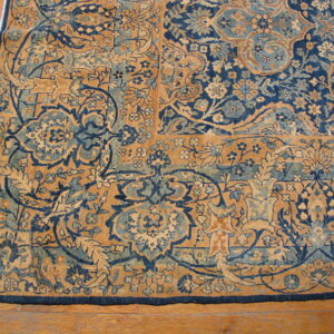 Close-up of a high-detail navy and gold floral rug border and corner on medium brown wood flooring.