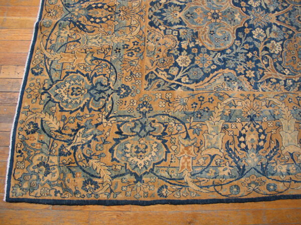 Close-up of a high-detail navy and gold floral rug border and corner on medium brown wood flooring.