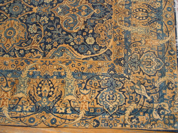 The detailed corner of a traditional rug featuring deep blue and tan floral designs on wood flooring.