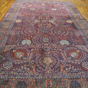 Ornate area rug featuring a burgundy background filled with blue and beige floral motifs, resting on hardwood.