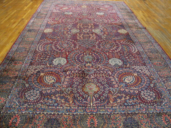 Ornate area rug featuring a burgundy background filled with blue and beige floral motifs, resting on hardwood.