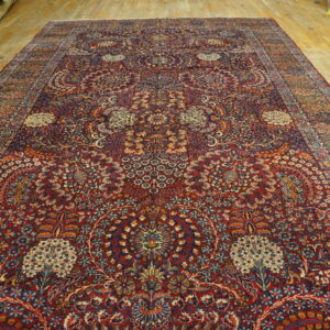 Ornate, dark red rug featuring a dense blue and cream floral design resting on wide wooden floorboards.