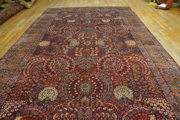 Ornate, dark red rug featuring a dense blue and cream floral design resting on wide wooden floorboards.