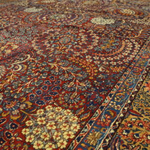 Angled view of a dense, traditional floral rug with fields of deep red and mustard gold.