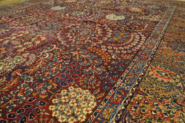 Angled view of a dense, traditional floral rug with fields of deep red and mustard gold.