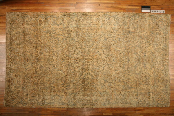 Rectangular tan rug with an intricate faded floral and vine pattern displayed on warm wood flooring.