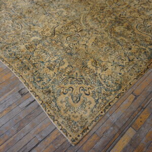 Close-up of a faded golden-yellow rug with intricate blue floral patterns on rustic, weathered wood planks.