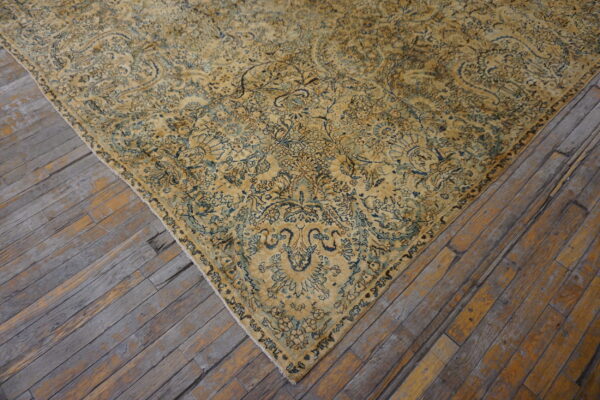 Close-up of a faded golden-yellow rug with intricate blue floral patterns on rustic, weathered wood planks.