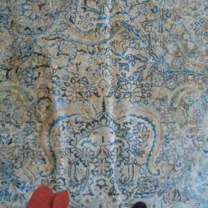 Distressed low pile rug featuring intricate blue and tan traditional floral and vine patterns.