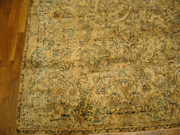 Muted golden rug with complex blue and dark brown floral motifs resting on brown hardwood planks.