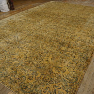 A large gold distressed rug with blue motifs lies on worn wood floors next to stacked white bags.