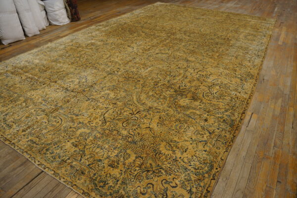 A large gold distressed rug with blue motifs lies on worn wood floors next to stacked white bags.