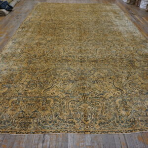 A large, faded ochre rug with dense blue and teal floral patterns lies on worn wood floors.