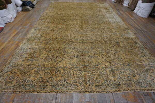 A large, faded ochre rug with dense blue and teal floral patterns lies on worn wood floors.