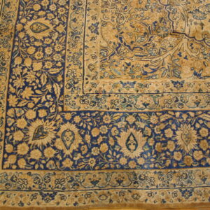Intricate floral rug corner featuring navy blue and beige patterns resting on a hardwood floor.