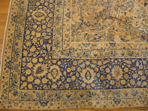 Intricate floral rug corner featuring navy blue and beige patterns resting on a hardwood floor.