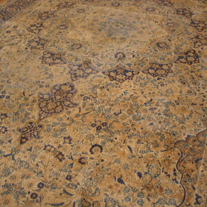 Faded tan and navy blue rug with a traditional medallion and dense all-over floral pattern.