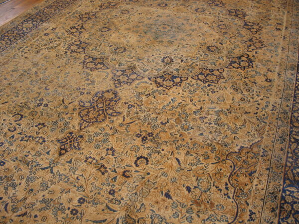 Faded tan and navy blue rug with a traditional medallion and dense all-over floral pattern.