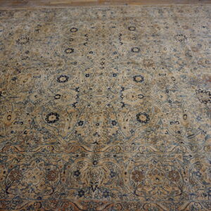 Intricate low-pile rug with beige, blue, and brown floral design lying flat on a distressed wood floor.
