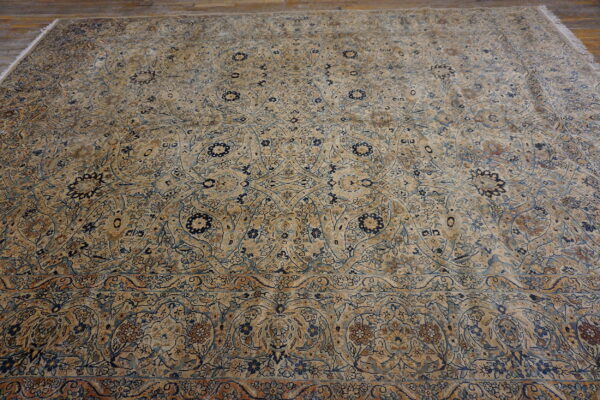 Intricate low-pile rug with beige, blue, and brown floral design lying flat on a distressed wood floor.