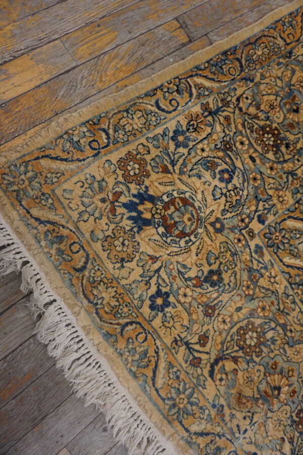 Gold rug with intricate blue and rust floral designs and fringe, set against worn wood planks.
