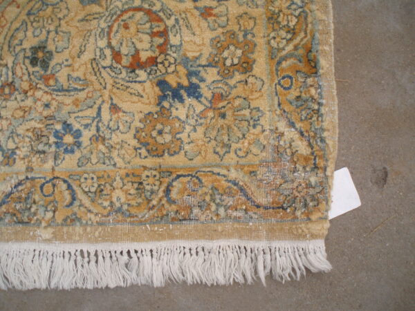 Tan floral rug detail with blue and terracotta patterns, white fringe, and a grey concrete background.