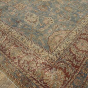 Traditional low-pile rug with a faded blue field and detailed red and tan border on rustic wood floors.