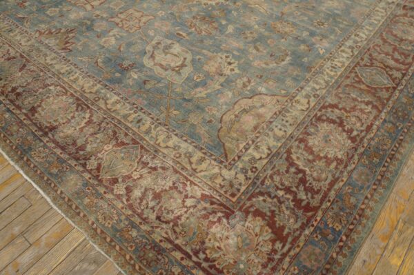 Traditional low-pile rug with a faded blue field and detailed red and tan border on rustic wood floors.