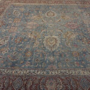 Faded blue rug with dense floral motifs and a maroon border rests on light wood floors.