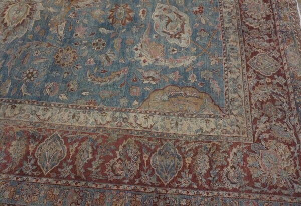 Muted blue rug with intricate floral patterns and multiple borders in faded red, beige, and tan.