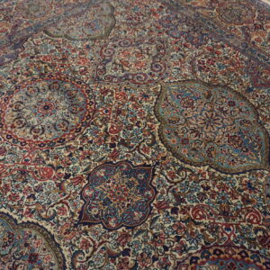 A dense patterned rug in red, navy, and light blue with an ivory background on a wood floor.