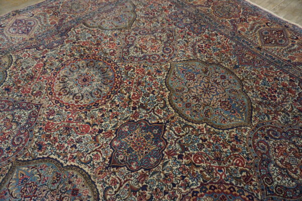 A dense patterned rug in red, navy, and light blue with an ivory background on a wood floor.