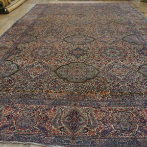 Large intricately patterned rug featuring reds and blues on a light ground, laid on wood floors.