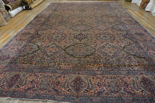 Large intricately patterned rug featuring reds and blues on a light ground, laid on wood floors.