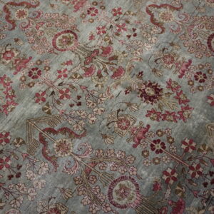 Intricate pink and burgundy floral pattern covers the subtly distressed, grayish-blue field of the rug.