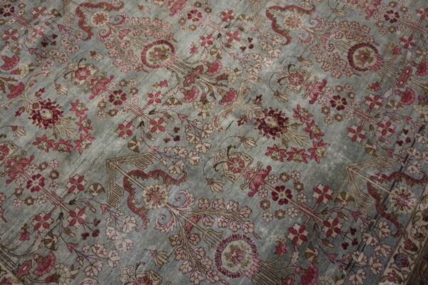 Intricate pink and burgundy floral pattern covers the subtly distressed, grayish-blue field of the rug.