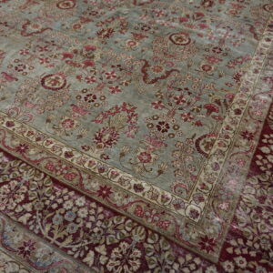Close up of a traditional rug with a dusty blue field and a dense maroon and floral border.