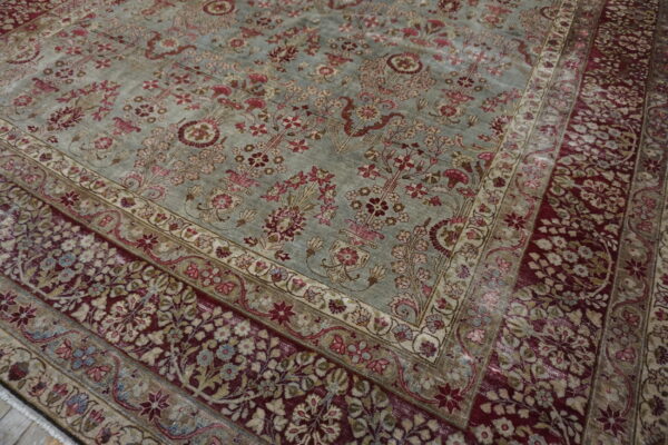 Close up of a traditional rug with a dusty blue field and a dense maroon and floral border.