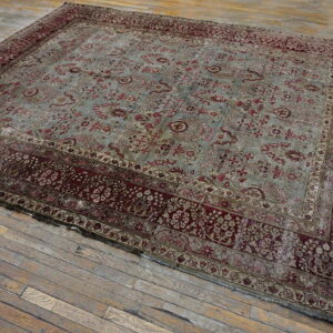Faded blue and deep red traditional rug with a wide border lying on distressed gray wood flooring.