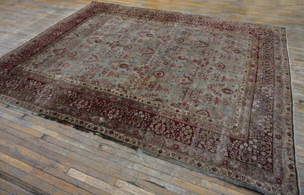 Faded blue and deep red traditional rug with a wide border lying on distressed gray wood flooring.
