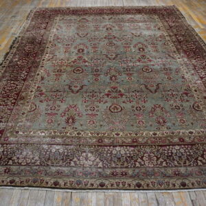 Ornate traditional rug with sage green field and burgundy floral borders displayed on wide wood planks.