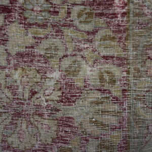 Close-up of a low-pile rug displaying burgundy and beige floral pattern over visible wood floorboards.