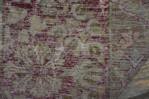 Close-up of a low-pile rug displaying burgundy and beige floral pattern over visible wood floorboards.
