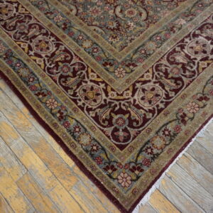 A burgundy and blue floral patterned rug corner rests on weathered wood planks.