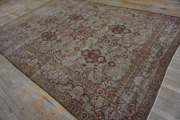 Ornate area rug in muted gray and burgundy with a low pile rests on distressed gray wood flooring.